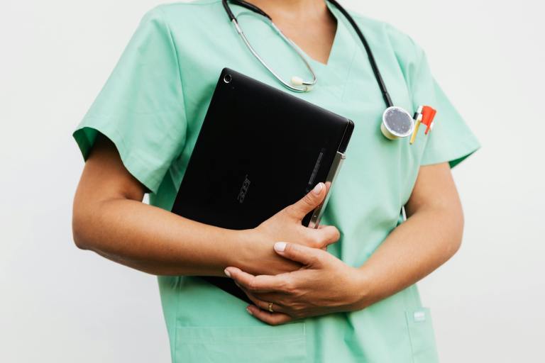 A nurse in green scrubbs holds a clipboard.