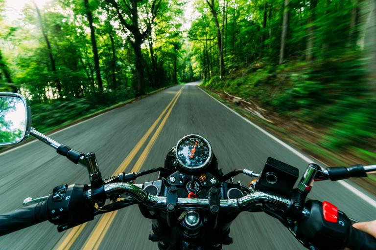 A motorcycle drives down a two-lane road surrounded by trees.