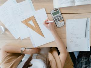 A student's works at a desk with papers and a calculator.