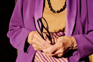 An elderly woman holds a pair of eyeglasses.