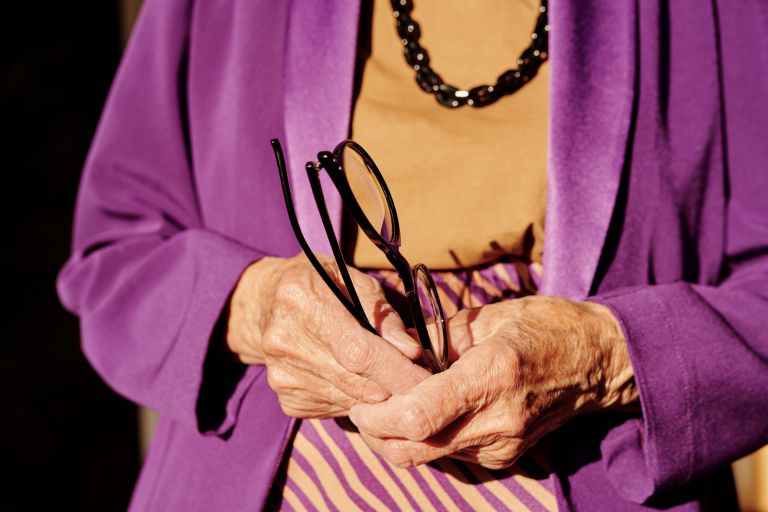 An elderly woman holds a pair of eyeglasses.