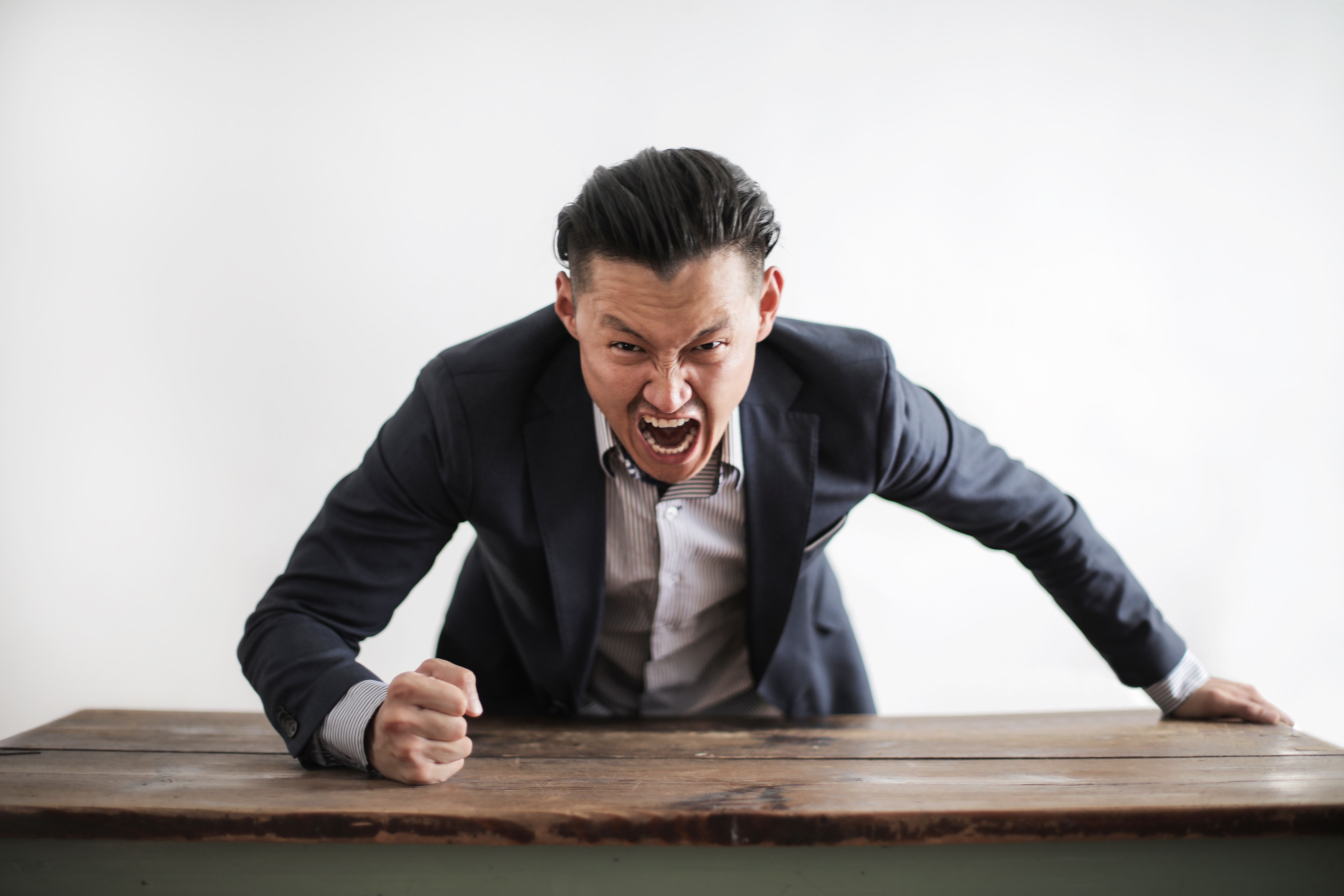 A man in a suit pounds a table with his fist in a fit of rage.
