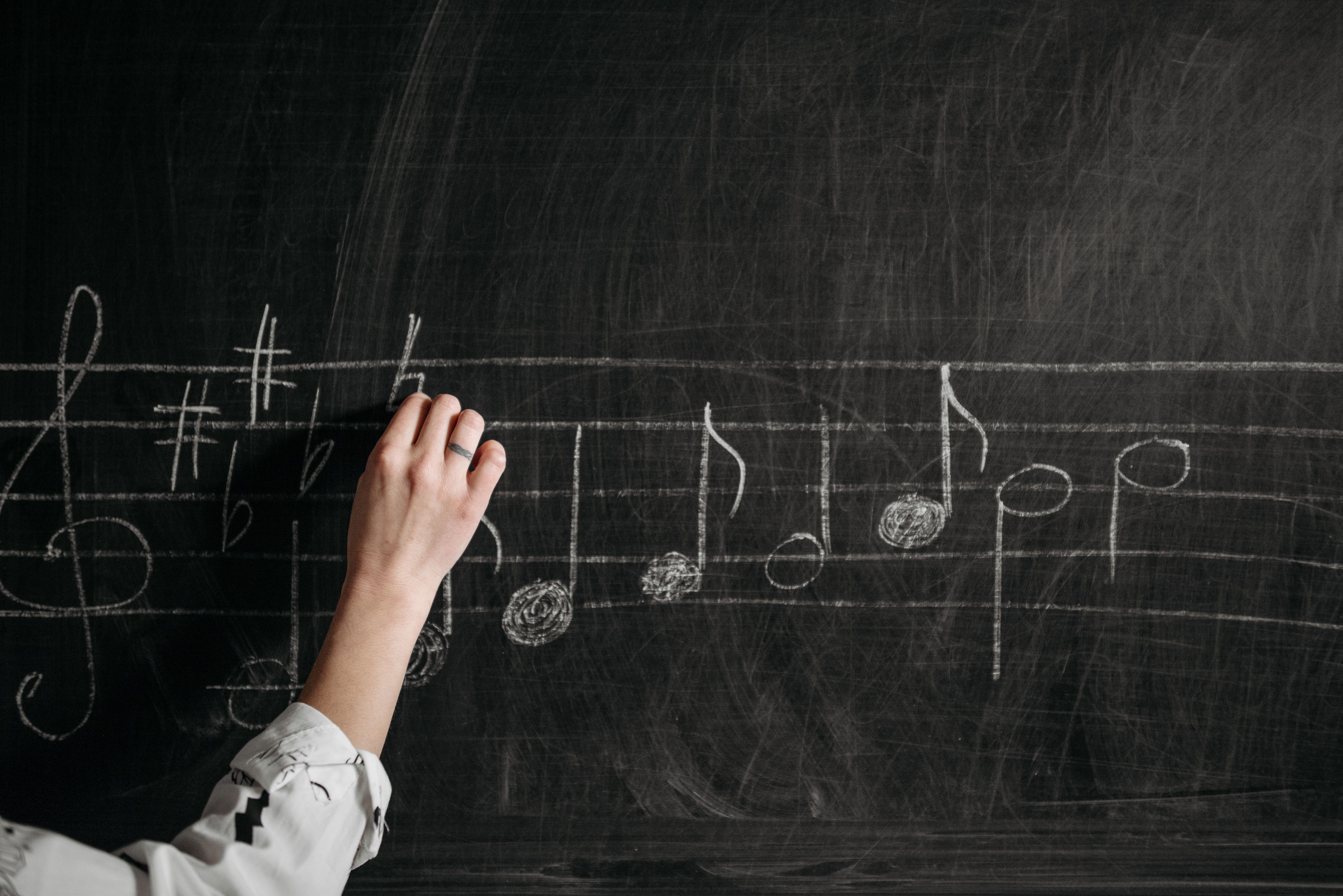 A person draws musical notes on a chalk board.