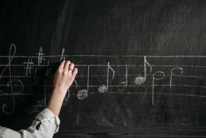 A person draws musical notes on a chalk board.