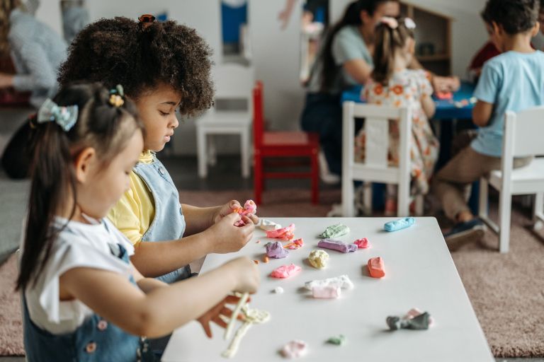 two kids stand at a table making crafts.