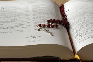 Rosary beads sit on an open copy of a bible.