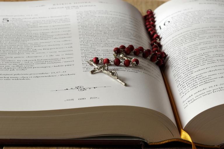 Rosary beads sit on an open copy of a bible.
