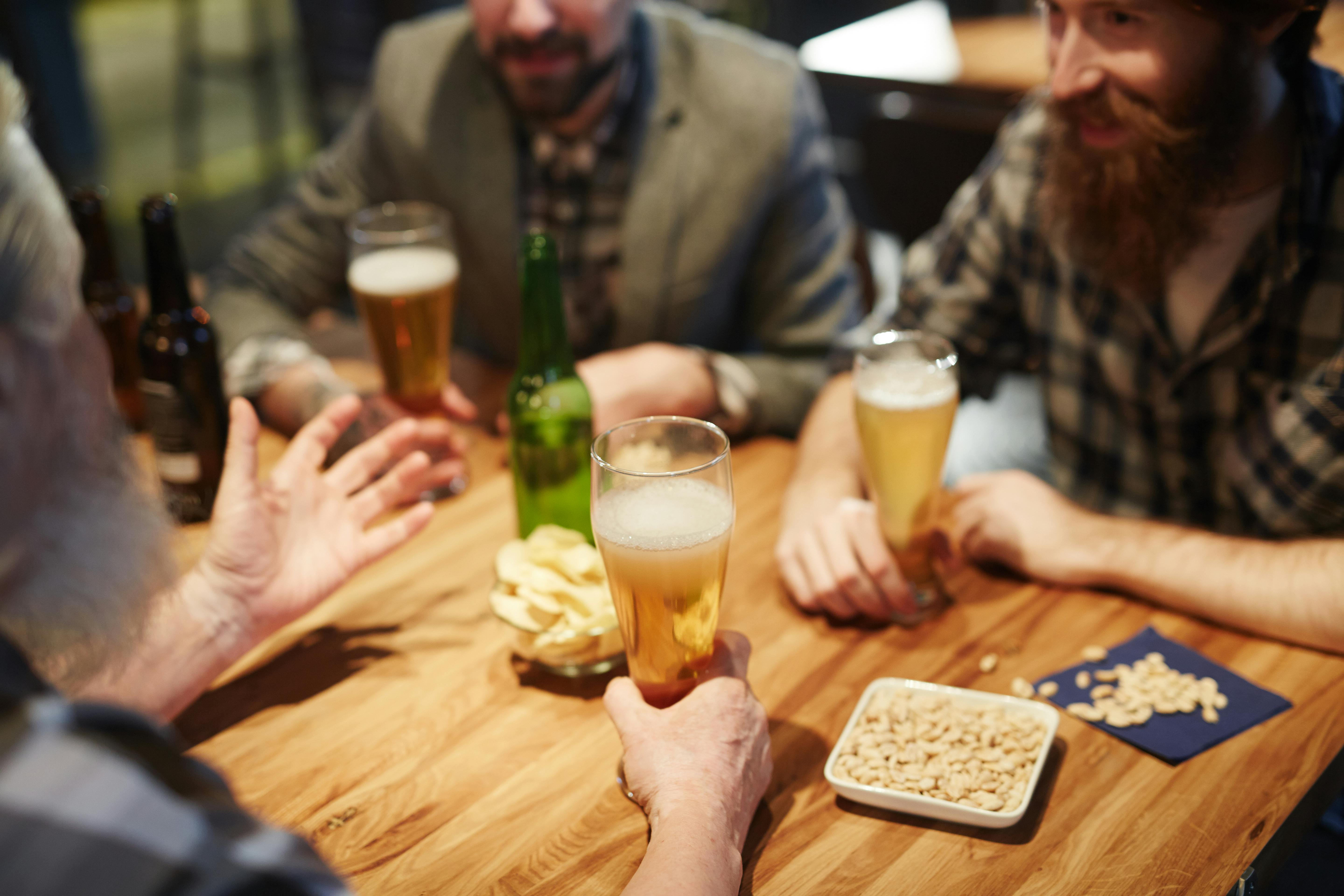 PEOPLE SIT AROUND A TABLE DRINKING BEER