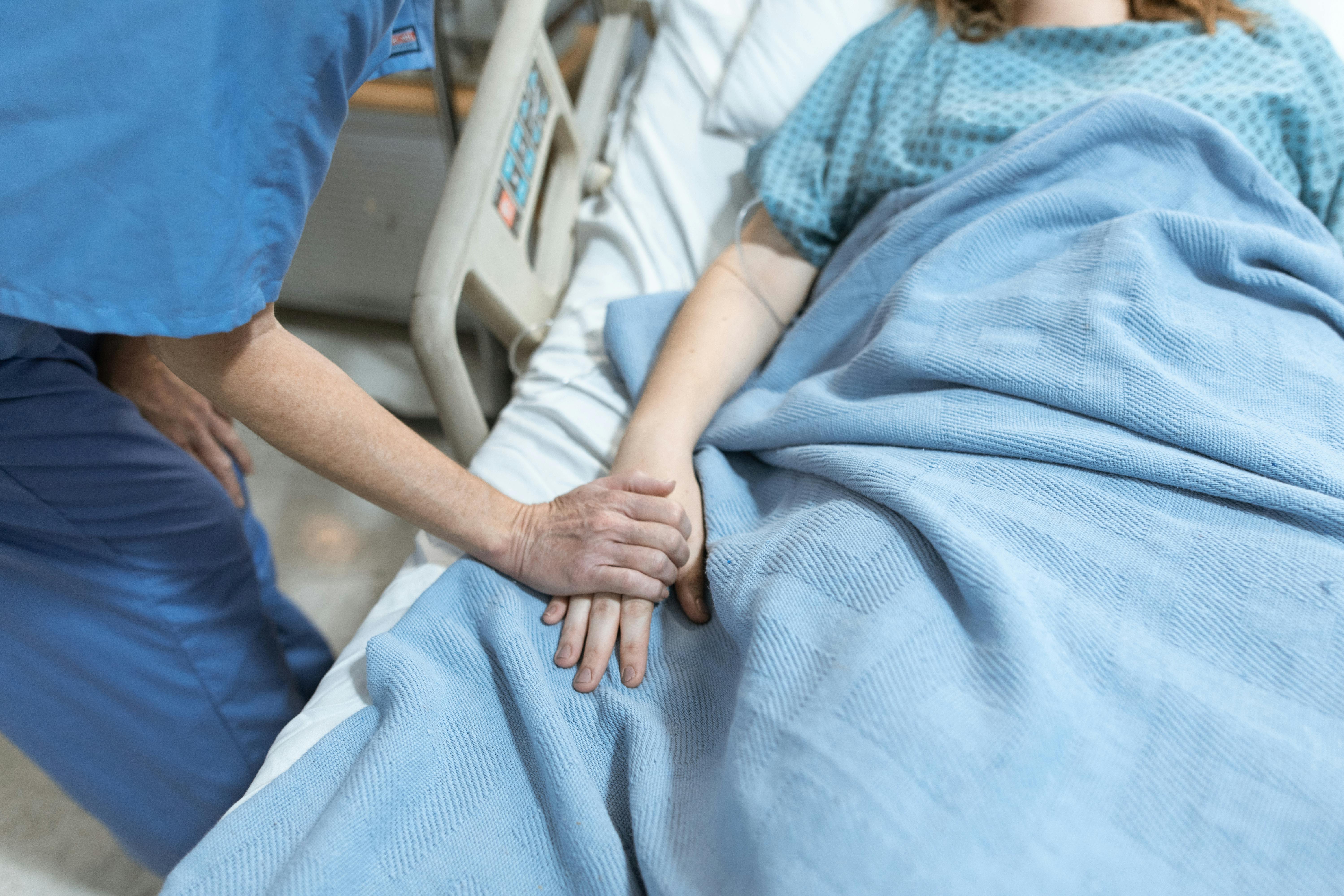 A nurse put her hand a patients hand in a hospital bed.