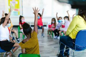 A group of children raise their hands at school.
