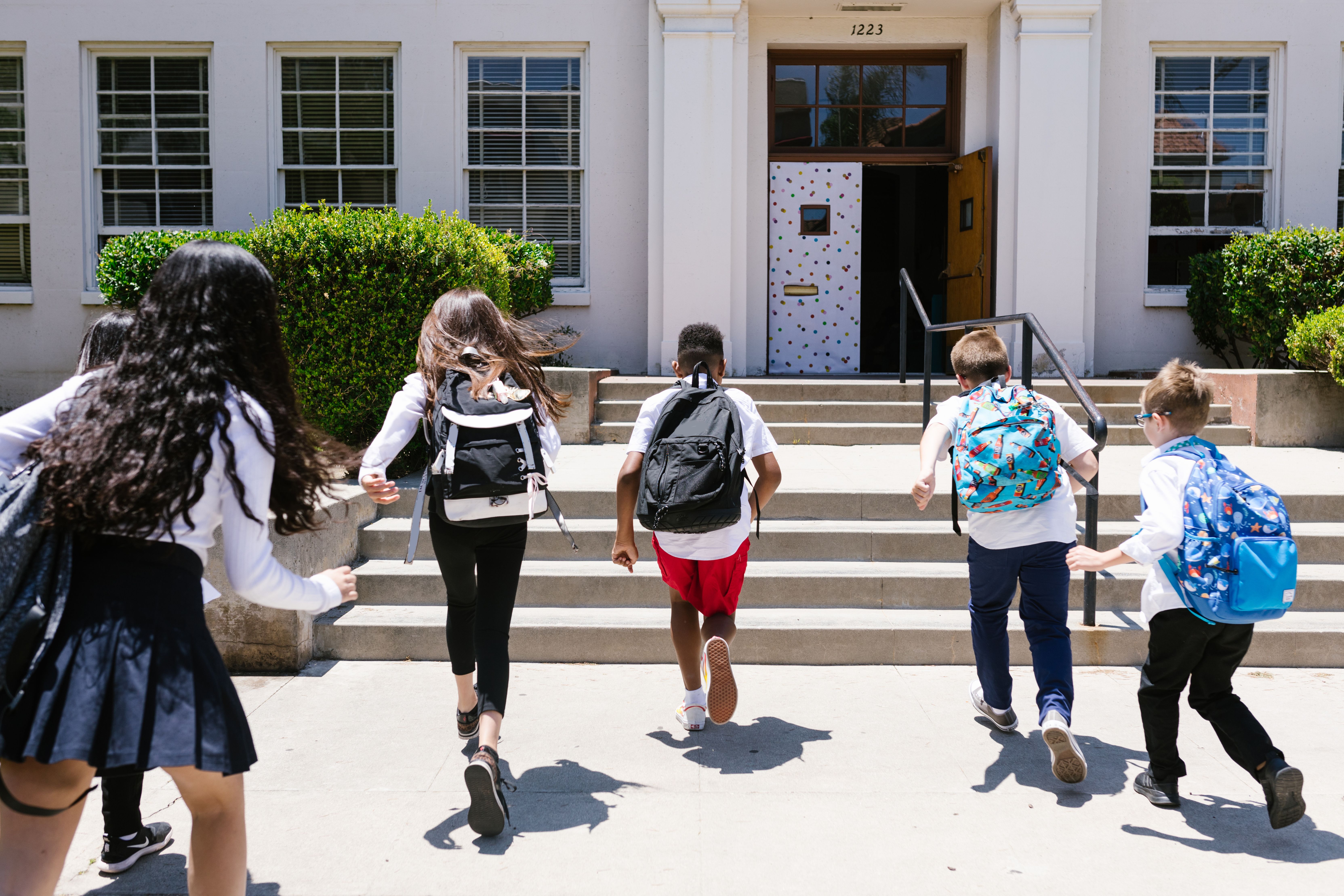 Children with backpacks run towards a school.