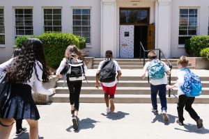 Children with backpacks run towards a school.