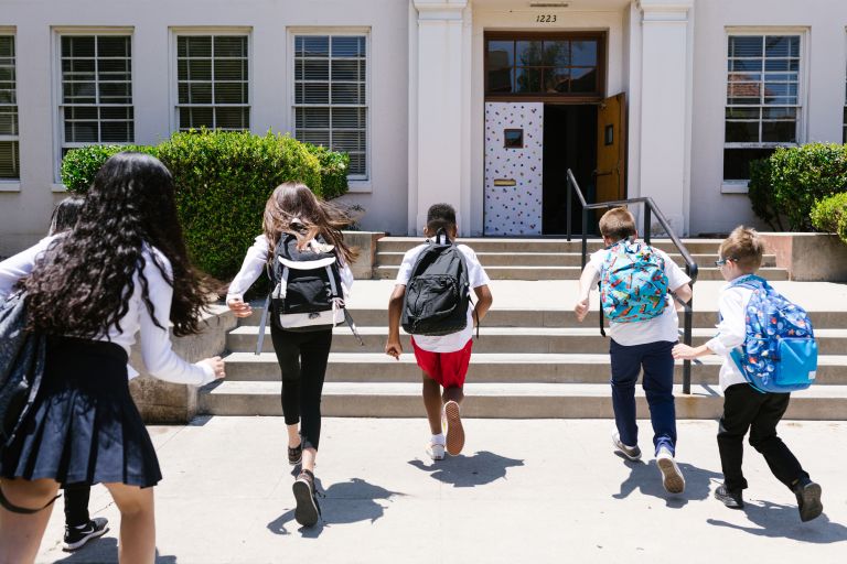 Children with backpacks run towards a school.