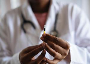 A person in a white coat holds up a syringe.