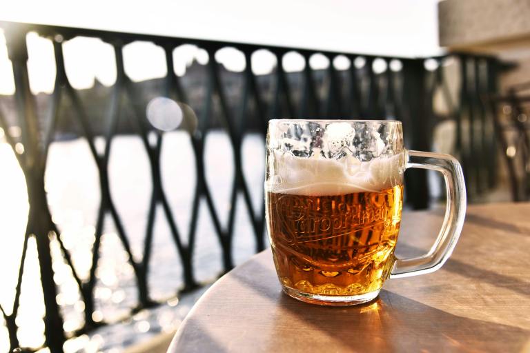 A glass of beer sits on a table by the water.