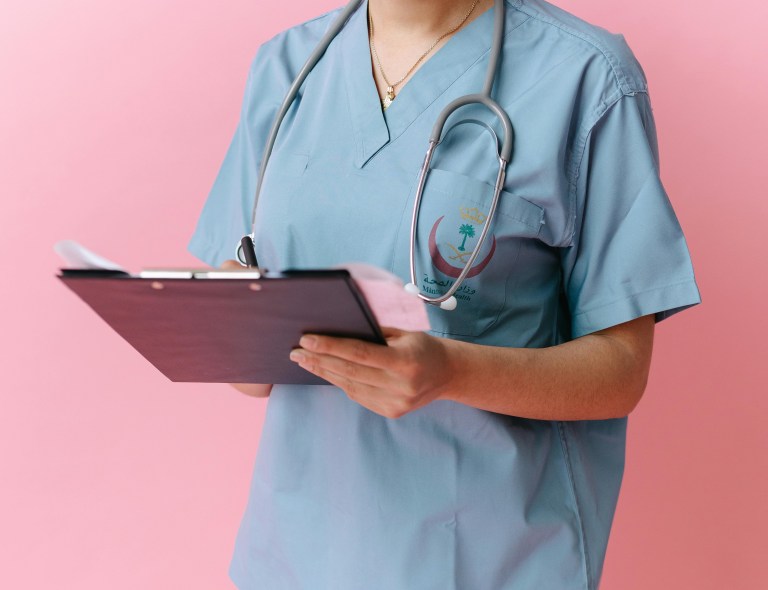 A wearing a stethoscope writes on a clipboard.