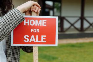 A realtor leans against a home for sale sign.