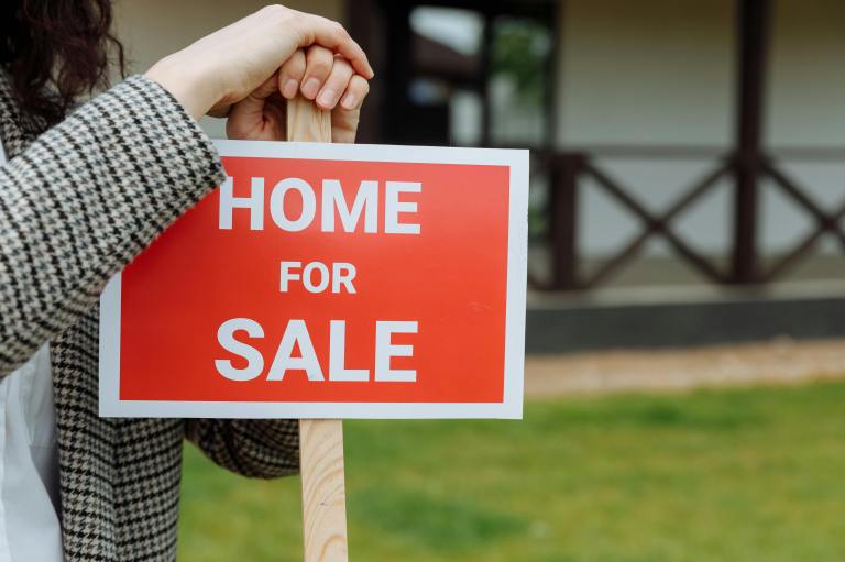 A realtor leans against a home for sale sign.