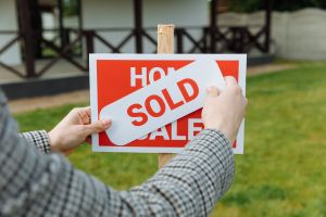 A person puts a sold sign on a real estate for sale sign.