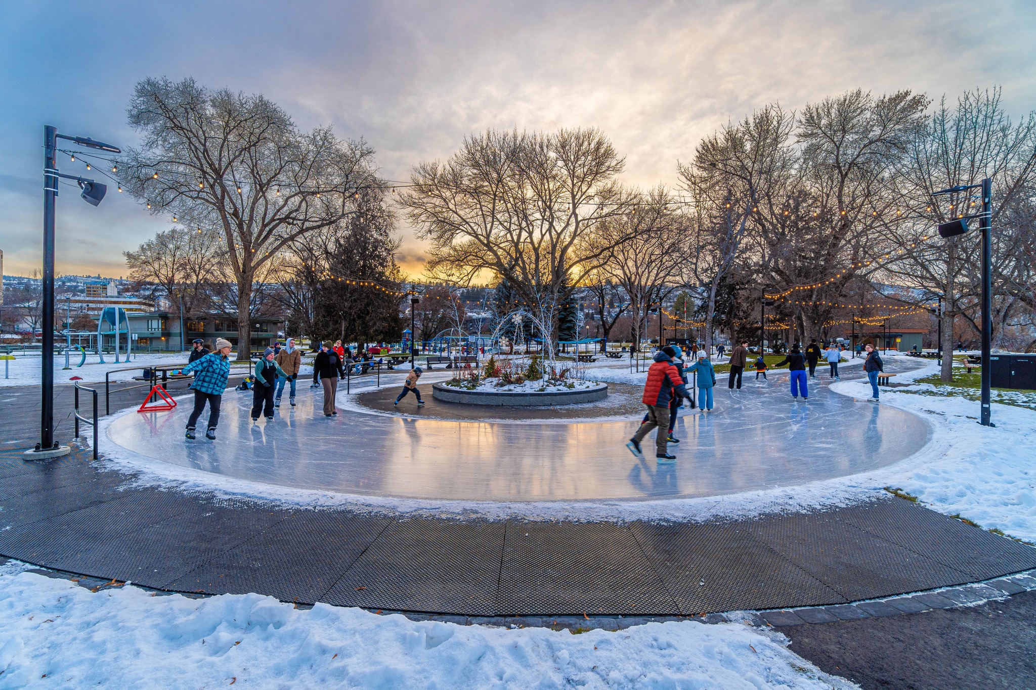 Families skate on an outdoor rink in a park.