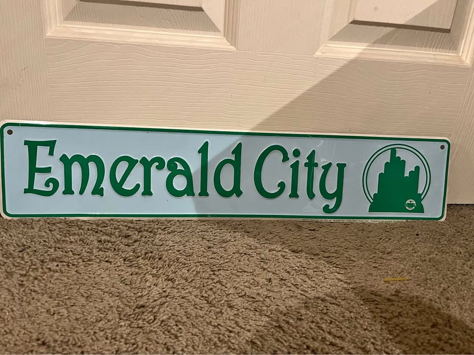 A metal sign reading Emerald City leans against a door.