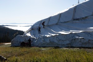 Three people climb a covered pile of snow using a rope.