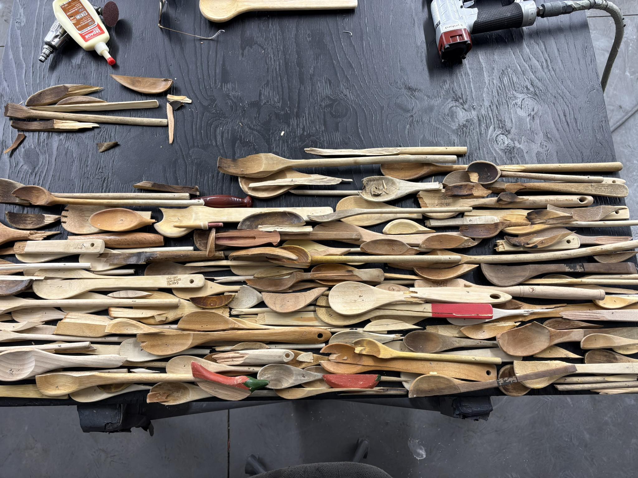 A pile of broken wooden spoons are spread out on a work table.