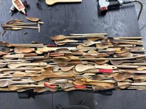A pile of broken wooden spoons are spread out on a work table.