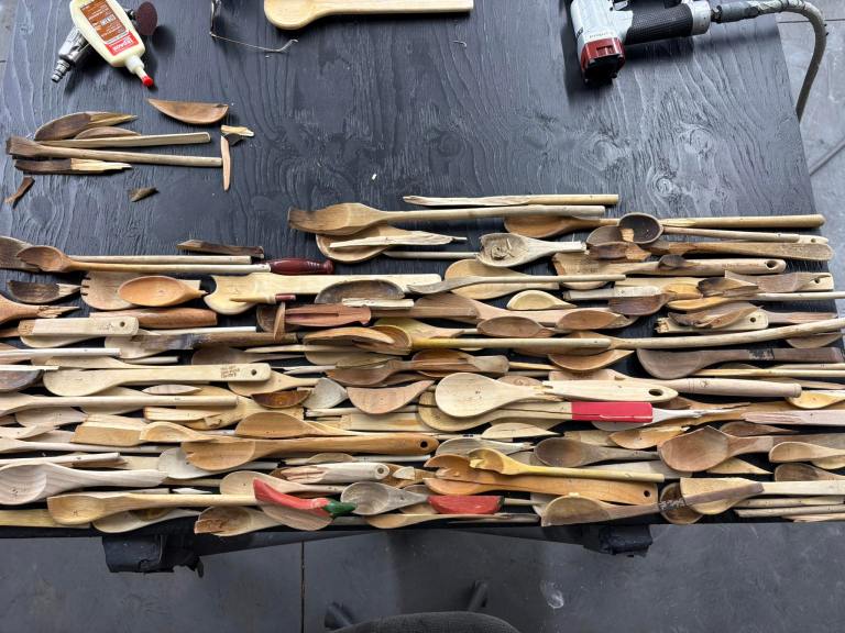 A pile of broken wooden spoons are spread out on a work table.