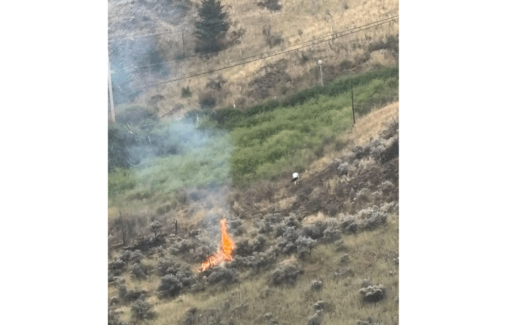 A man walks away from a grassfire on a hillside.