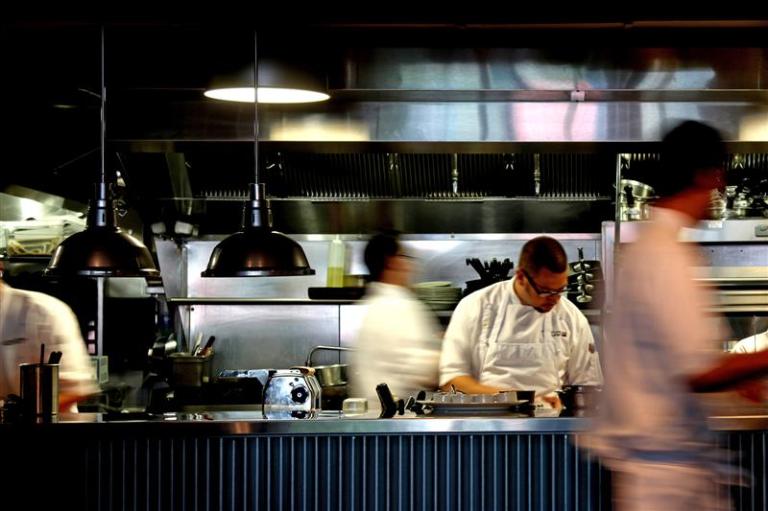 A chef preparing a dish while blurred people move quickly around him.