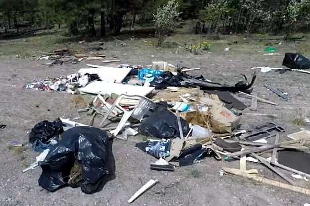 A pile of garbage is scattered on the side of a dirt road.