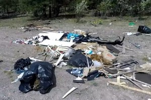 A pile of garbage is scattered on the side of a dirt road.