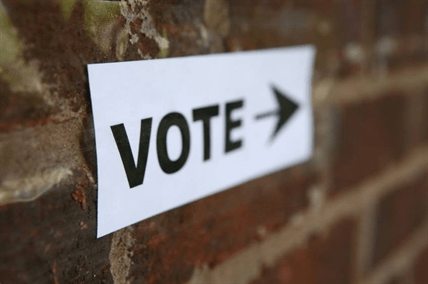 A sign on a brick wall has the word vote and an arrow.